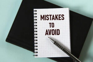 MISTAKES TO AVOID words in a white notebook against the background of a black notebook with a pen